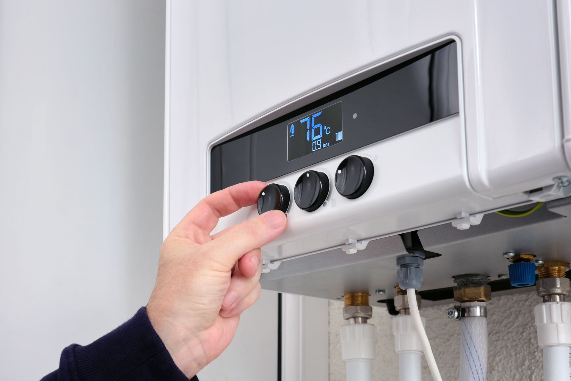 A man sets the temperature on a modern digital gas boiler in a house.